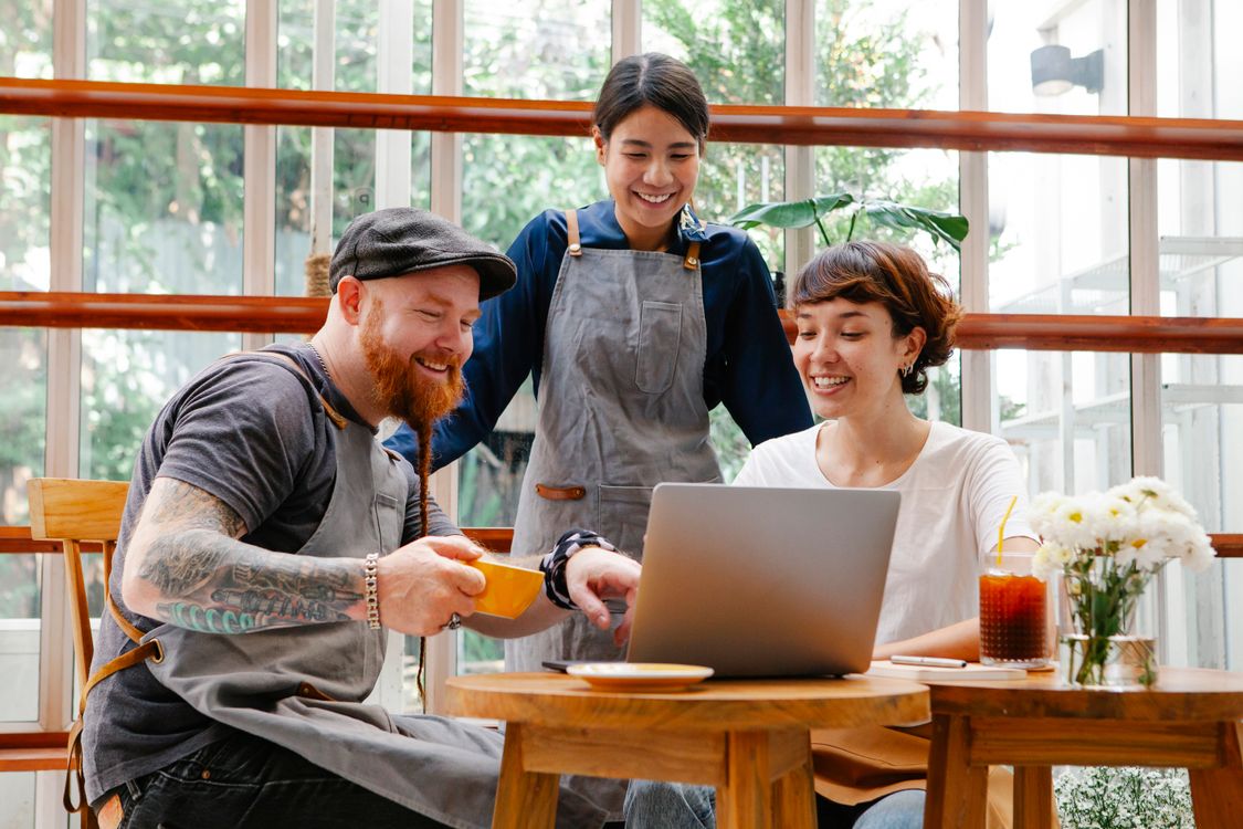 Colleagues collaborating over a laptop in a cafe, representing a freelance client call