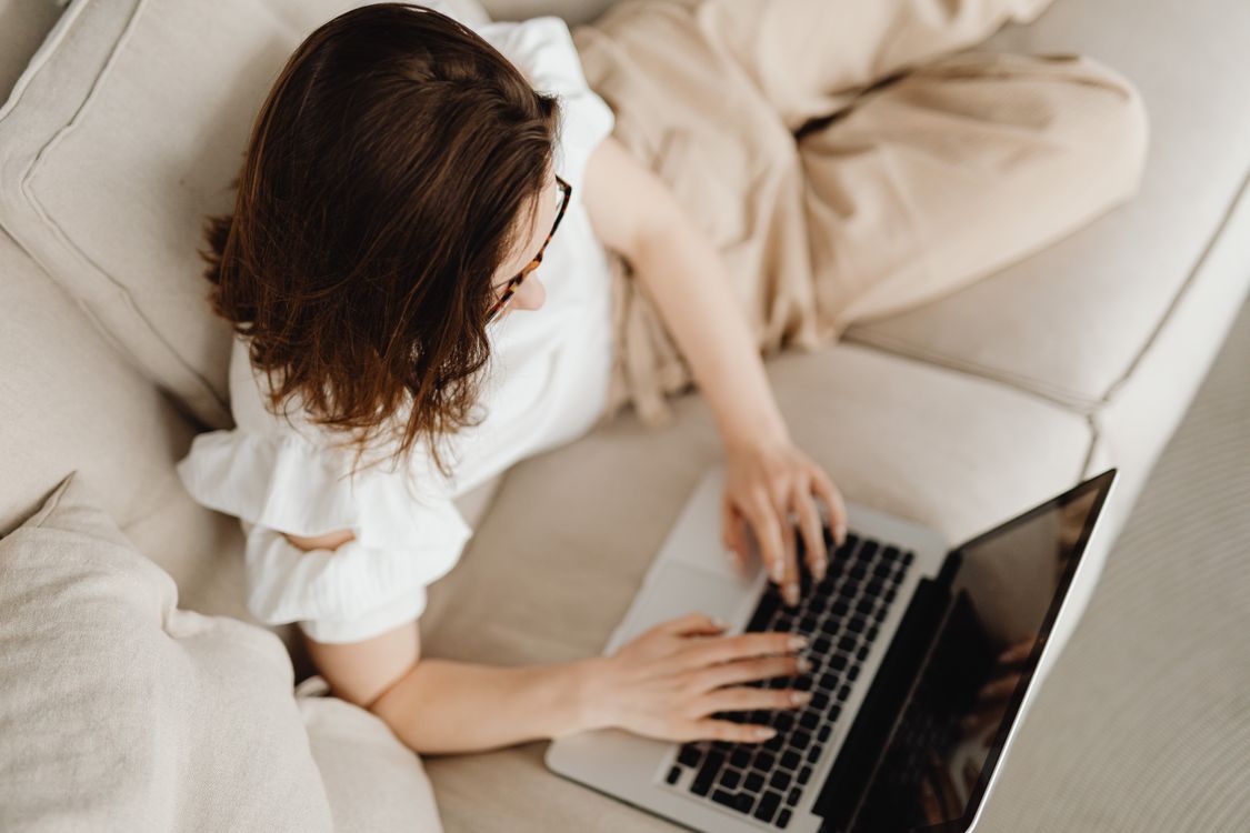 Person typing on a laptop while relaxing on a couch, representing flexible remote IT work