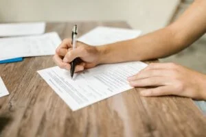 Hand filling out a government job application form with a pen